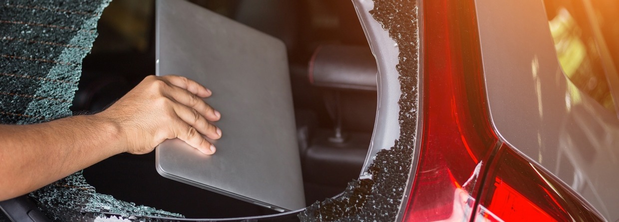 Auto inbraak; hand haalt via gebroken achterraam een laptop uit de auto